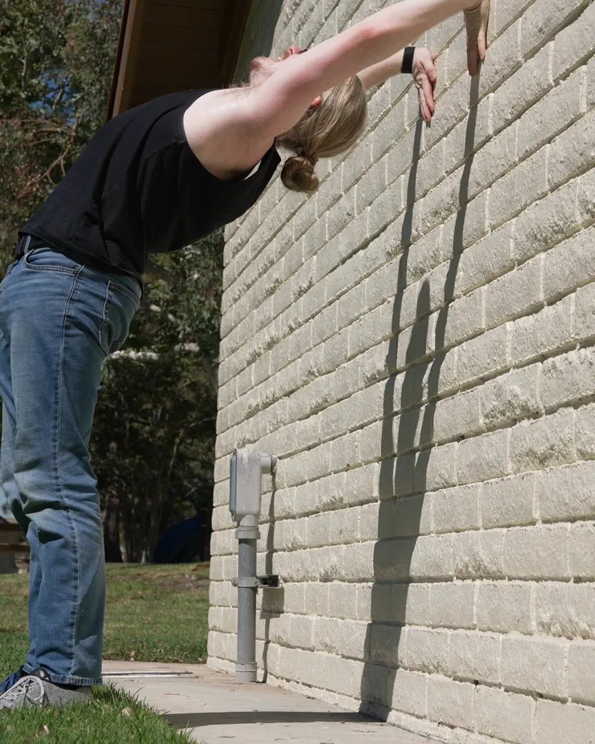 David arching back against a wall, hands walking down it