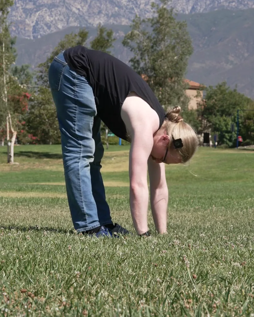 David folded all the way forward, palms on the grass, mountains behind him